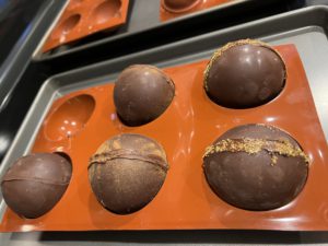 Five spheres of chocolate sitting in a tray of six half-sphere molds